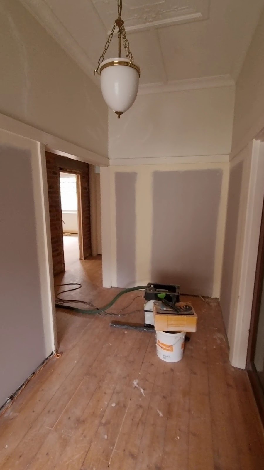 Period hallway with a pendant light, walls patched and sanded, plaster bucket on the floorboards